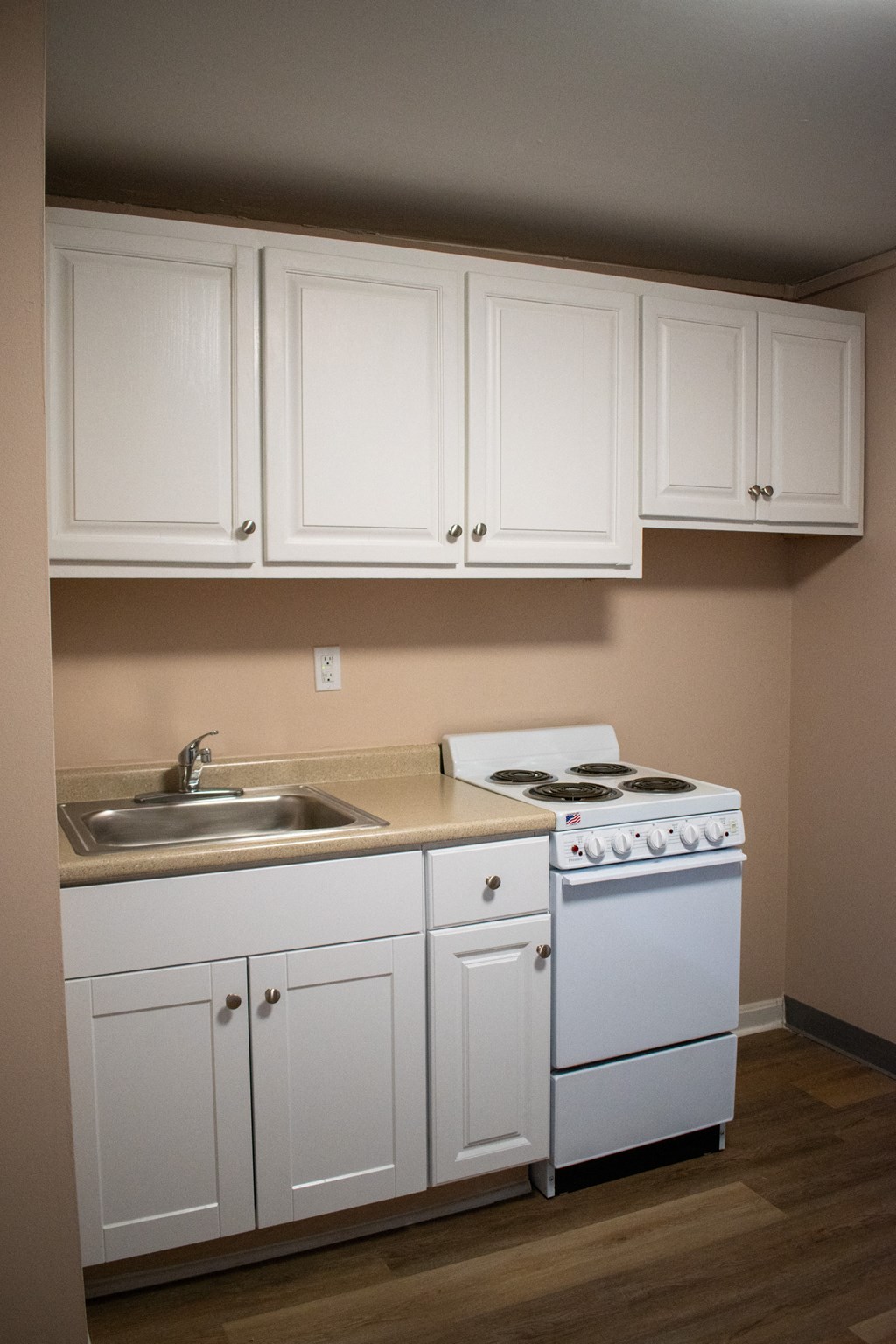 an empty kitchen with white cabinets and a stove and sink