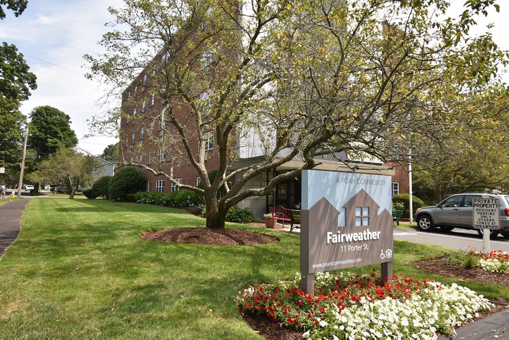 a sign in the front yard of a house with a tree