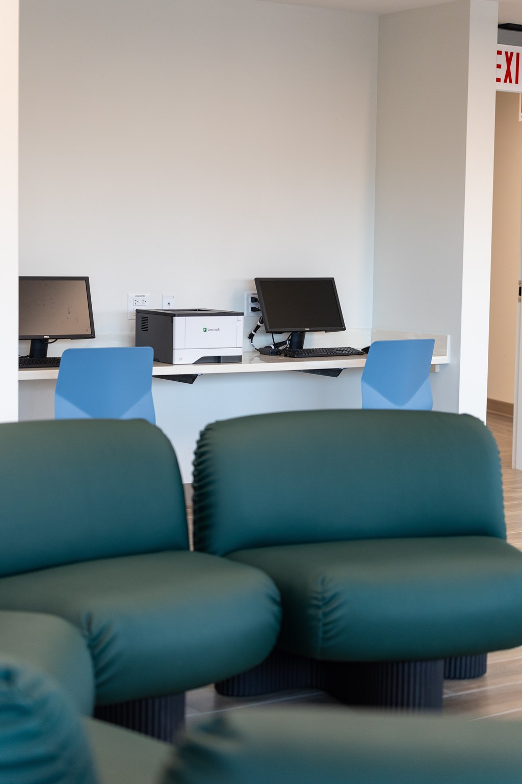 Two green chairs are in front of a desk with two computers.
