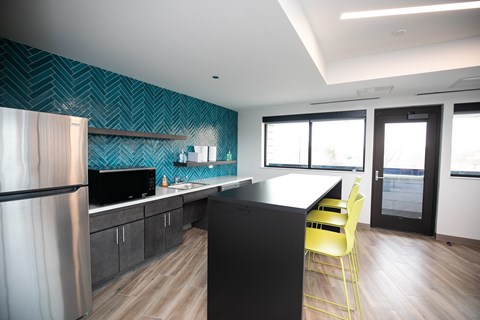 A modern kitchen with a black counter and yellow chairs.