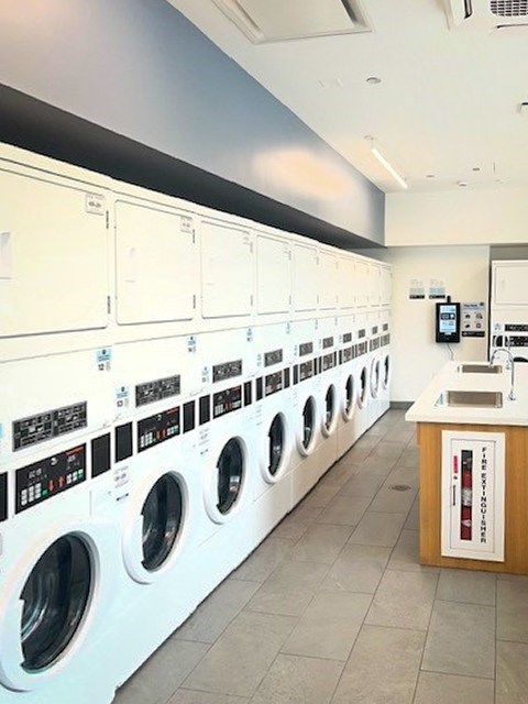 A row of white washing machines are lined up in a laundromat.