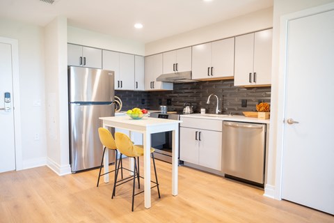 a kitchen with white cabinets and stainless steel appliances and a white island with yellow chairs