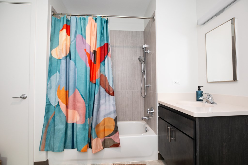A shower curtain with a colorful abstract design hangs over a white bathtub in a bathroom.