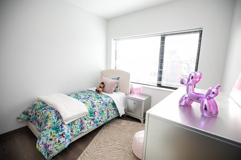 A bedroom with a floral bedspread and a pink unicorn figurine on the desk.