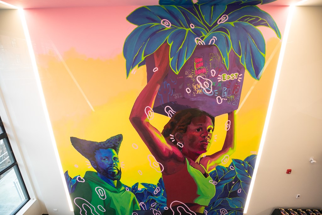 A woman is carrying a large pineapple on her shoulder.