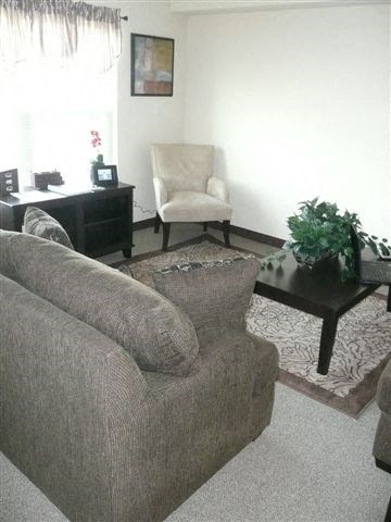 A living room with a grey couch, a white chair, a black coffee table, and a painting on the wall.