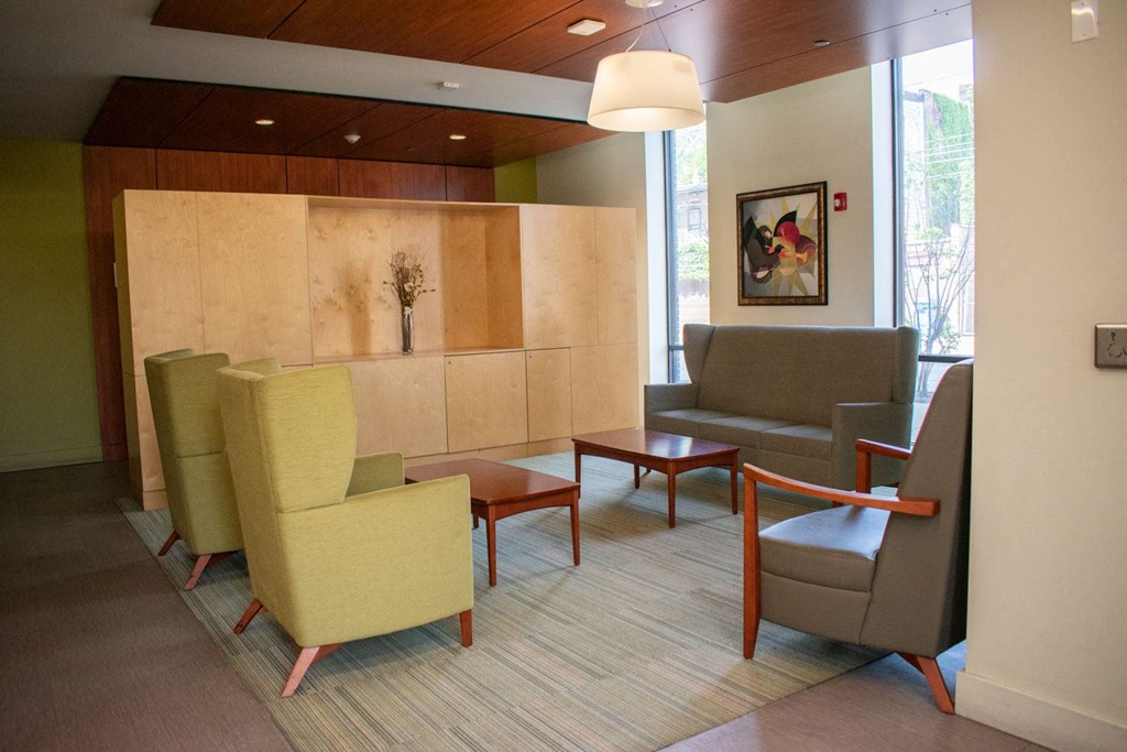 a seating area with chairs and tables in front of a wall with a painting on it