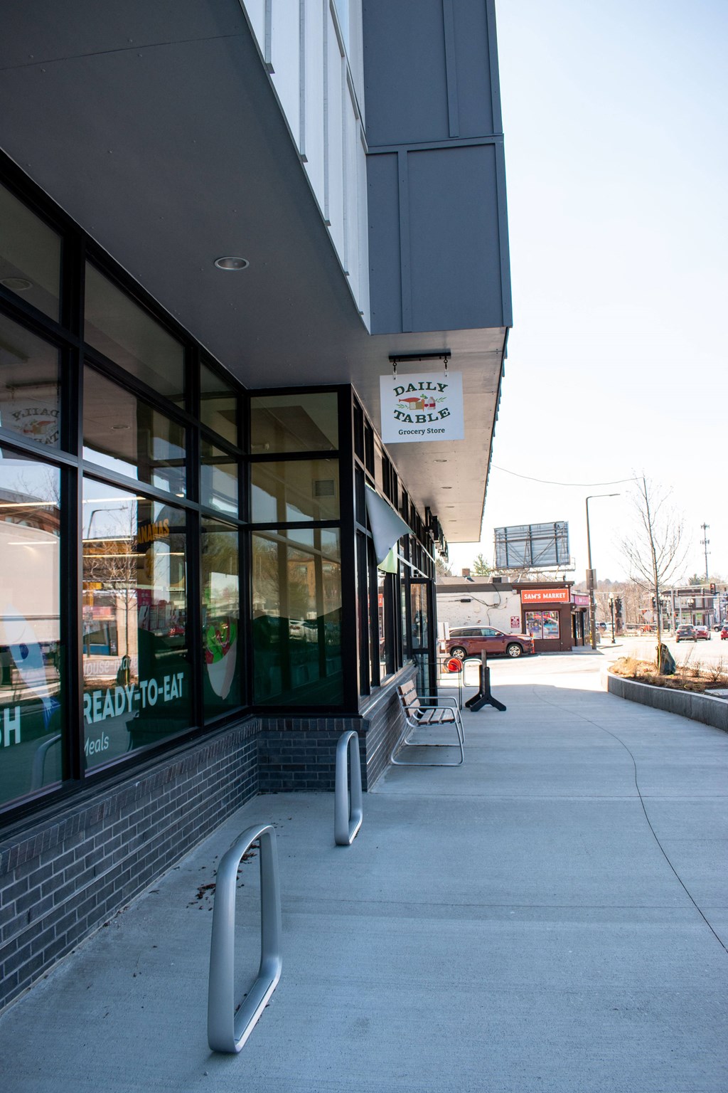 a sidewalk in front of a building with glass windows and a bench