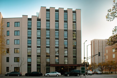 A large building with a lot of windows is in the middle of a street with cars parked in front.