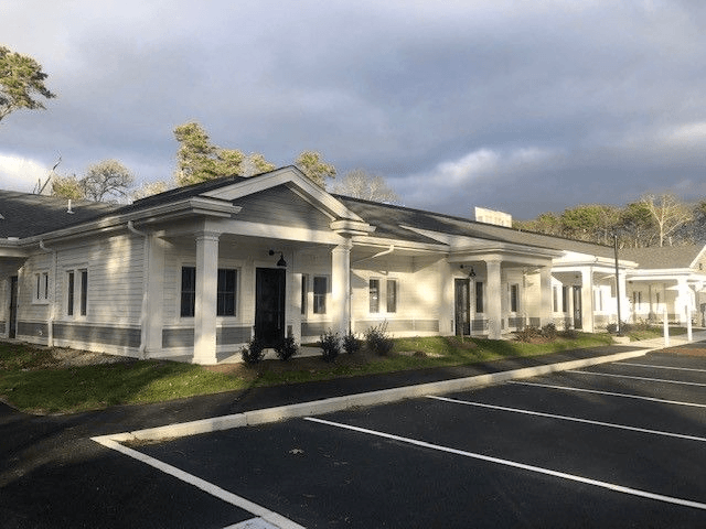 A white building with a black door and windows is surrounded by a parking lot.