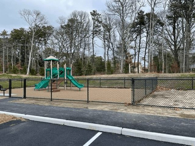 A playground with a green slide and a black fence.