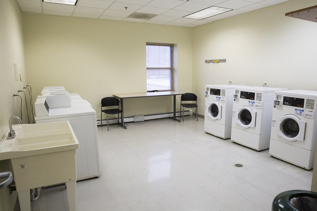a washer and dryer room with a row of washing machines and a table
