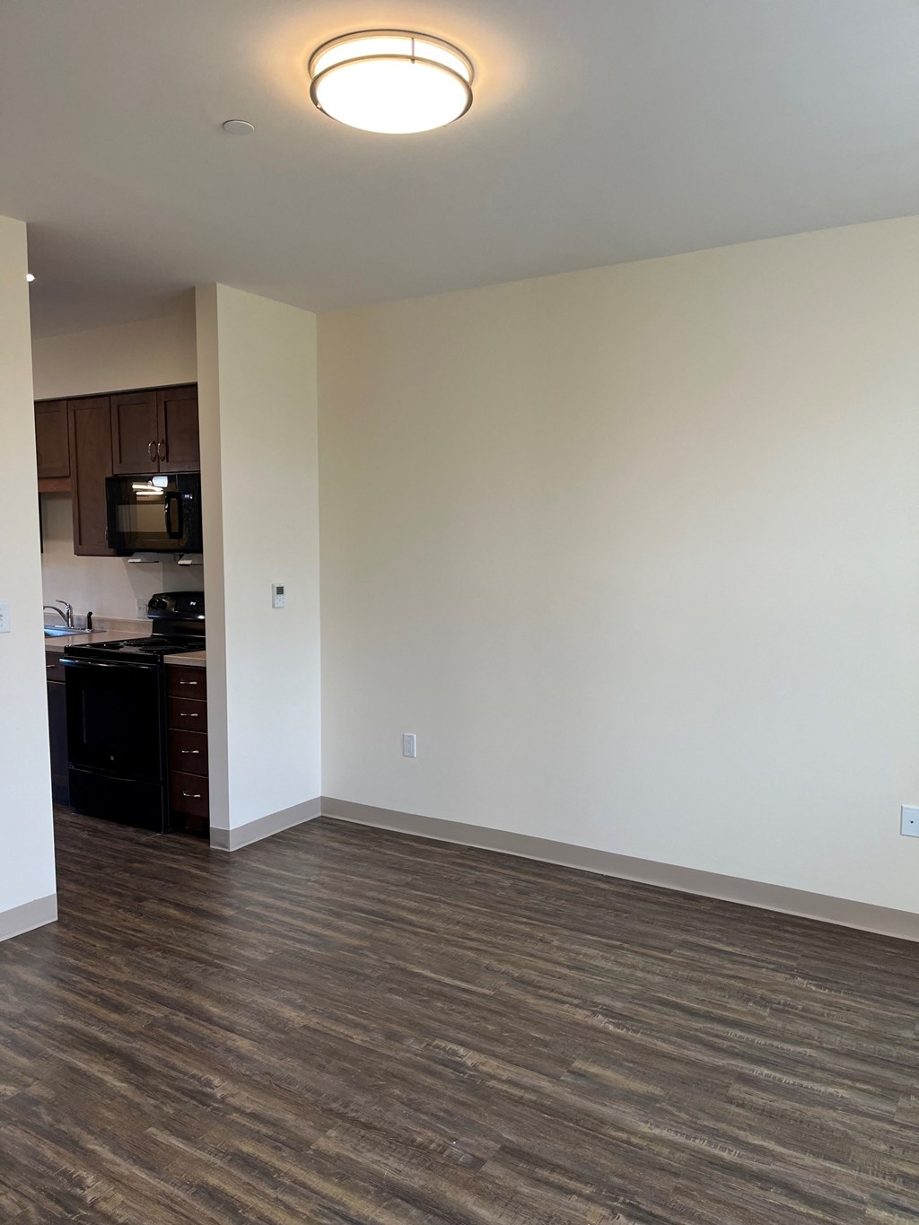 an empty living room with wood flooring and a kitchen