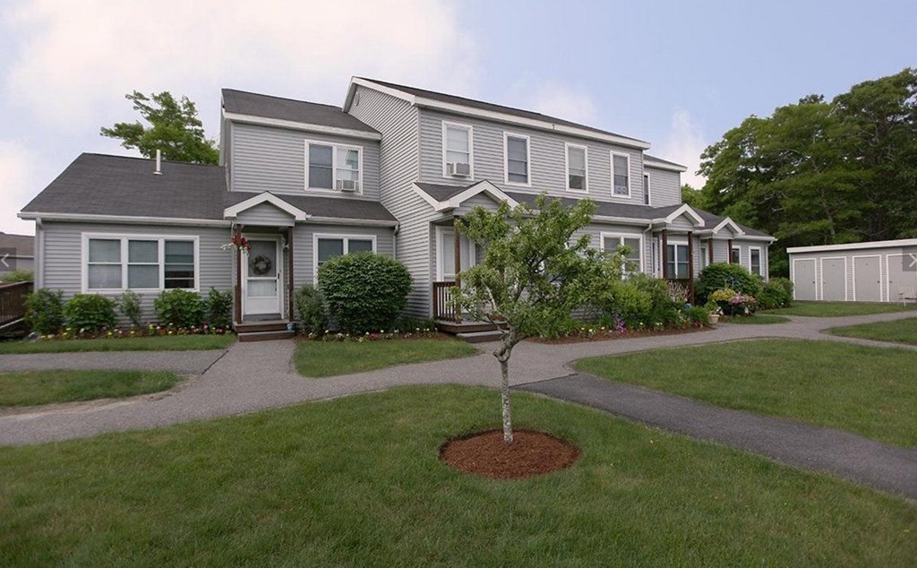 A grey house with a tree in front of it.