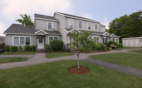 A grey house with a tree in front of it.