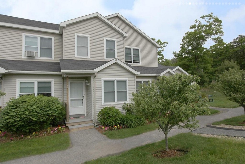 A house with a grey roof and white walls with a small tree in front of it.