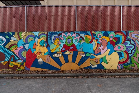 A mural of people sitting around a table is painted on a wall.