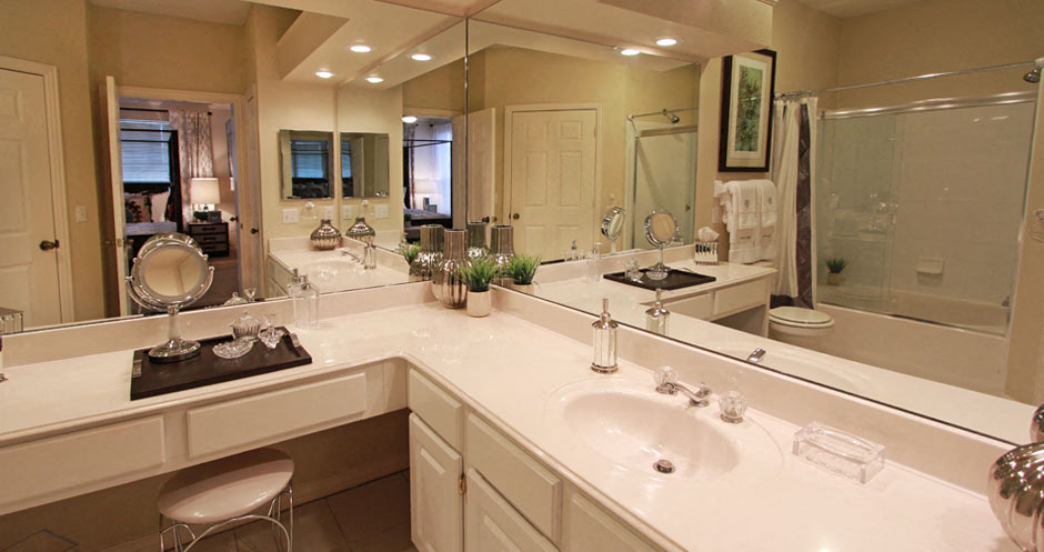 Luxury apartments with white cabinets, linen closet, extra cabinet space, cultured marble vanity, built-in vanity, roman tub with glass door and shower, and porcelain tiled floor at The Biltmore Apartments in Omaha, Nebraska