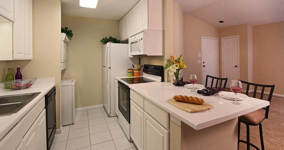 Bright white kitchen with lots of cabinet space, lots of counter space, spacious living room, breakfast bar, and washer and dryer in unit at LionsGate Apartments in Lincoln, Nebraska