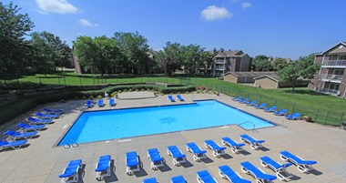 Huge swimming pool with spacious sundeck, poolside lounge chairs, beautiful landscaping, scenic views, lots of trees at LionsGate Apartments in Lincoln, Nebraska