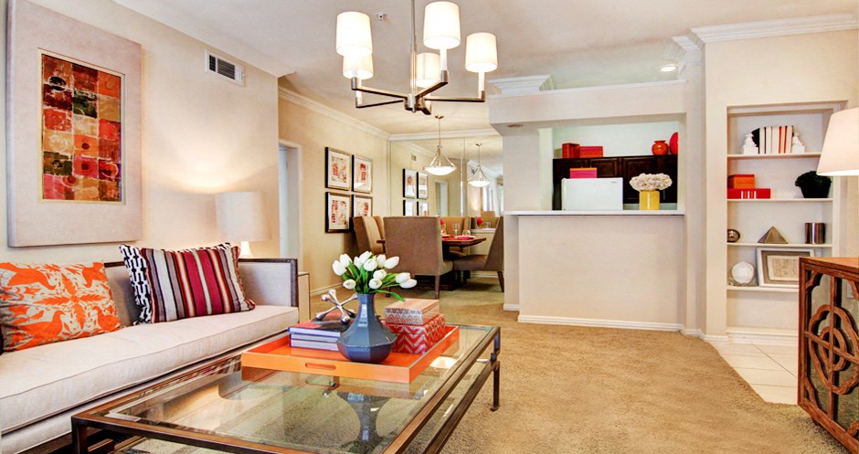 Spacious living room with built-in bookshelves, crown molding, dining room with mirrored accent walls, 9-foot ceilings, and breakfast bar at Tuscany Apartments in Houston.