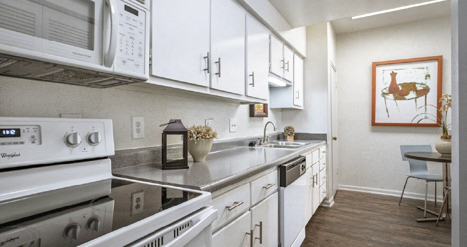 Bright white kitchen with wood plank floors, extra cabinet space and counter space at Woodlake on the Bayou Apartments