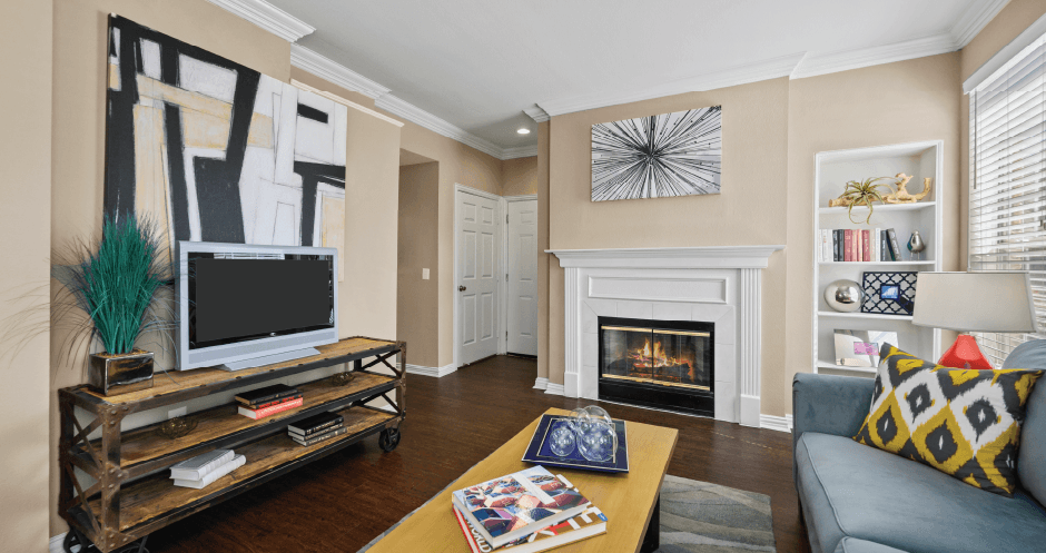 Spacious living room with wood-burning fireplace with glass doors, built-in shelves and hardwood floors at Tuscany Park Apartments in Houston.