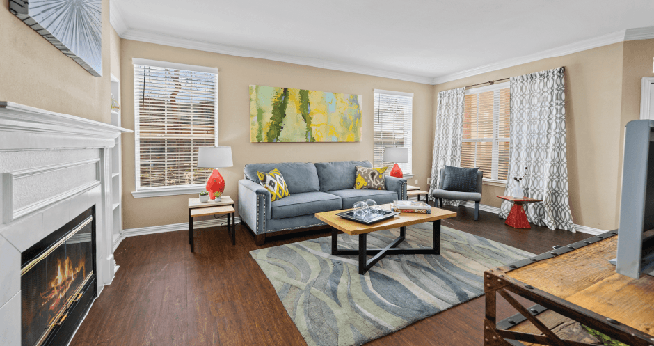 Spacious living room with wood-burning fireplace with glass doors, hardwood floors, and oversized windows Tuscany Park Apartments in Houston.