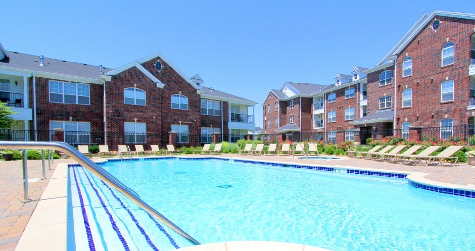 Luxury apartments with red brick exteriors, swimming pool, pool-side lounge chairs, beautiful landscaping, and scenic views at Rockledge Oaks Apartments in Lincoln, Nebraska