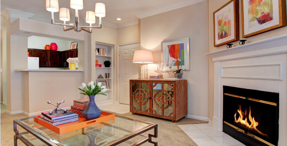 Spacious living room with wood-burning fireplace with glass doors, crown molding, and built-in bookshelves at Tuscany Apartments in Houston.