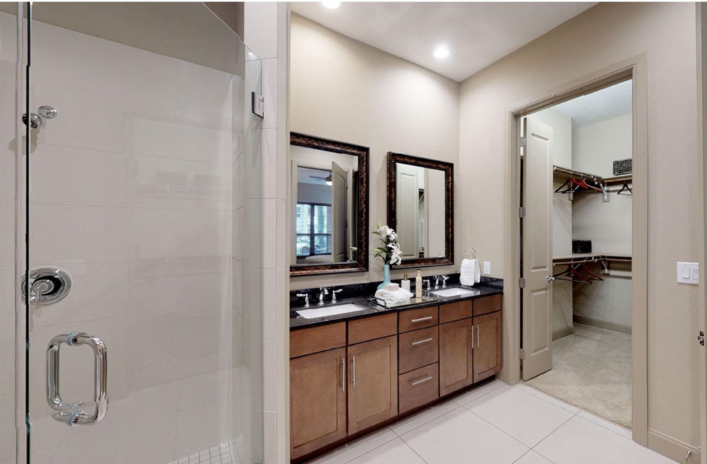 Luxury apartments with spacious master bathroom with oval soaking tub, separate shower with glass enclosure, and double sink with granite slab vanity top at Tuscany Walk Apartments in Houston.