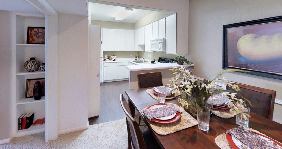 Spacious dining room with built-in bookshelf, bright kitchen with white cabinets, and breakfast bar at Woodlake Oaks Apartments in Houston