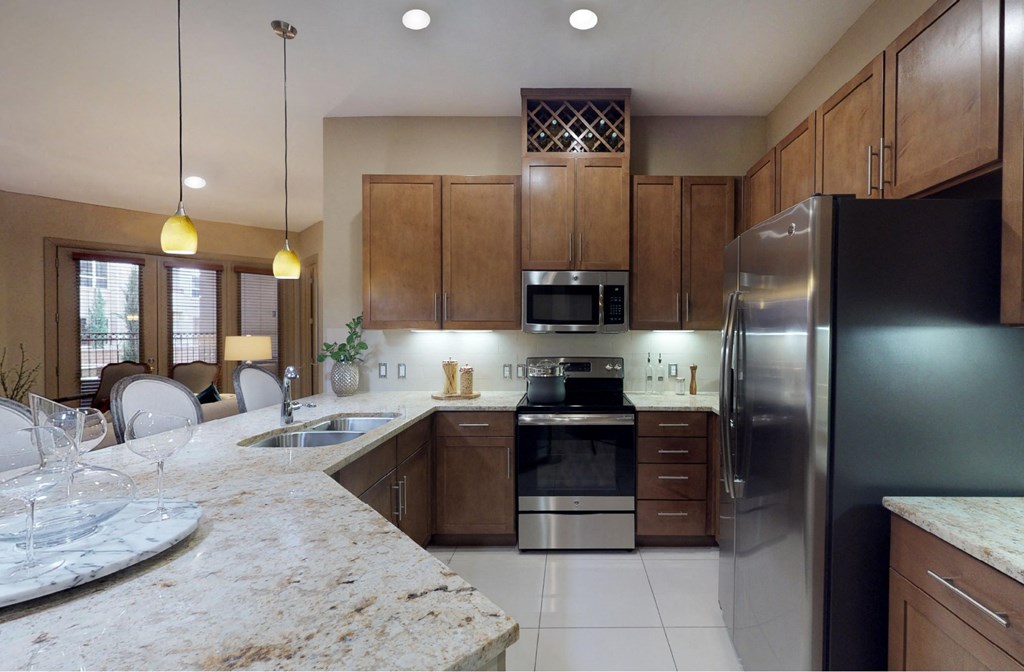 Luxury apartments with spacious kitchen and built-in wine rack, granite countertops, kitchen island, stainless steel appliances, and designer tile backsplash at Tuscany Walk Apartments in Houston Texas.