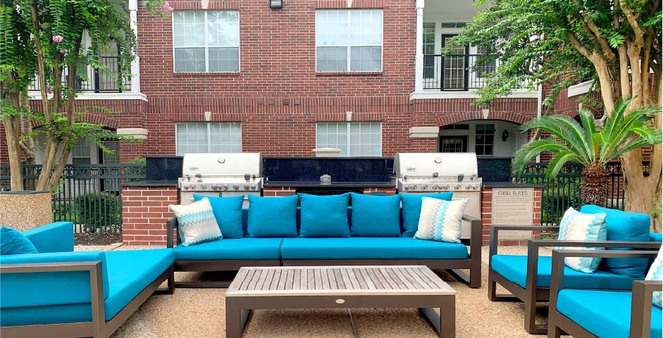 Luxury apartments with brick exteriors, pool-side lounge seating, and grilling area at Tuscany Apartments in Houston.