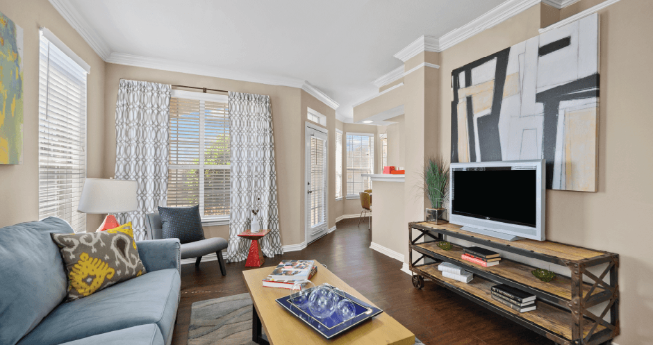 Spacious living room with wood-burning fireplace with glass doors, ceiling fan, oversized windows and French door at Tuscany Park Apartments in Houston.