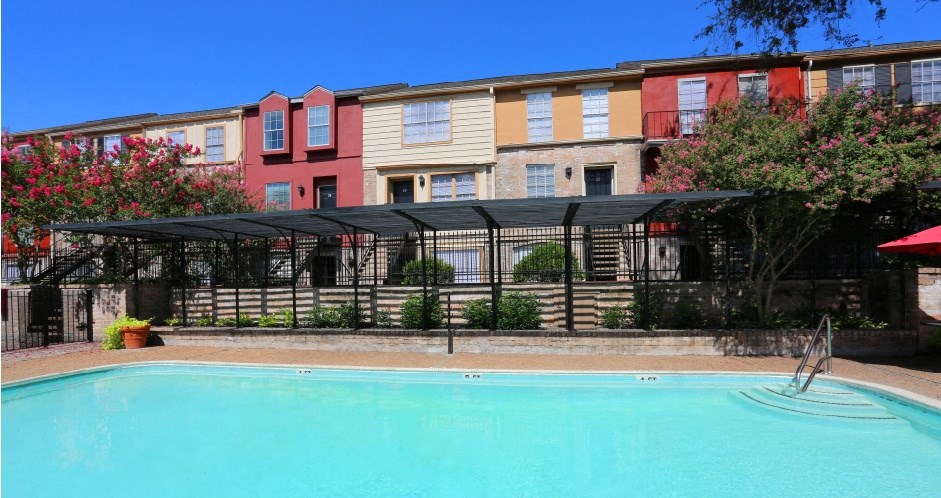 Large swimming pool with lush landscaping and colorful townhomes at Briarwood Apartments in Houston, Texas.