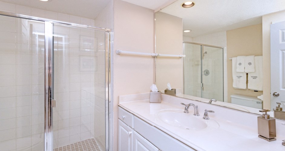 Bathroom with white cabinets, glass shower, extra cabinet space, walk-in shower, porcelain floor, and tiled shower at Embassy Park Apartments in Omaha, Nebraska