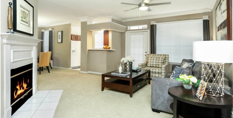 Spacious living room with wood-burning fireplace, crown molding, 9-foot ceilings, breakfast bar, ceiling fan, refrigerator with water and ice dispenser at Tuscany Apartments in Houston.