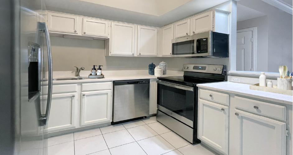 Spacious bright white kitchen with white cabinets, stainless steel appliances, side-by-side refrigerator, and tiled floor at Prestonbridge Apartments in North Dallas