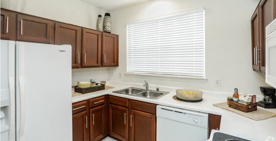 Spacious kitchen with honey brown toned cabinets with modern silver hardware, and white appliances including a double sided fridge with water and ice dispenser.