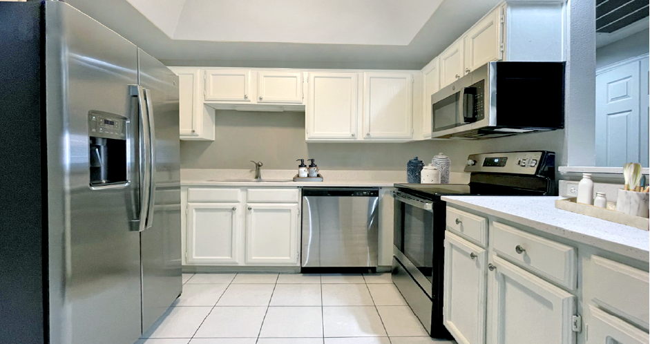 Spacious bright white kitchen with white cabinets, stainless steel appliances, side-by-side refrigerator, and tiled floor at Prestonbridge Apartments in North Dallas