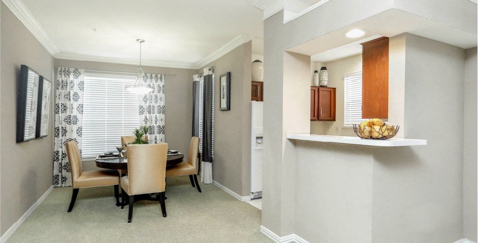 Spacious dining room and kitchen with honey brown toned cabinets with modern silver hardware, and white appliances.