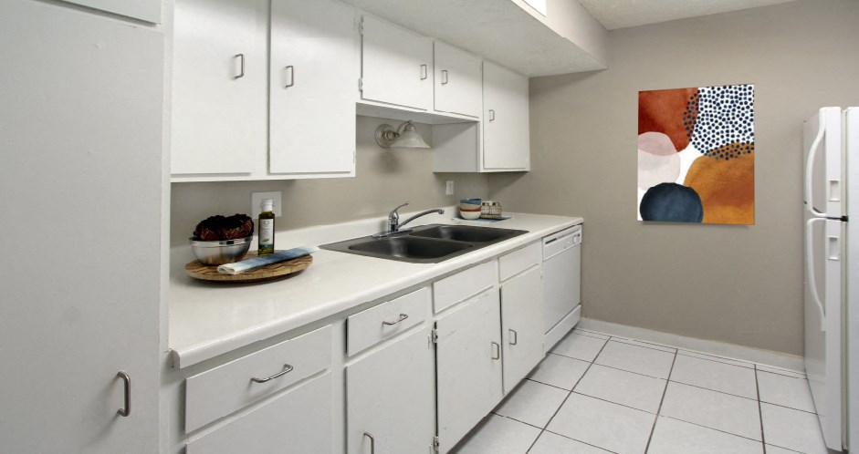 Bright white kitchen with gray wall color, white kitchen cabinets, lots of cabinet space, lots of counter space, and porcelain tile floors at The Inverness Apartments in La Vista, Nebraska