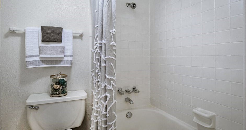 Bright white bathroom with white shower tiles at Woodlake Oaks Apartments in Houston