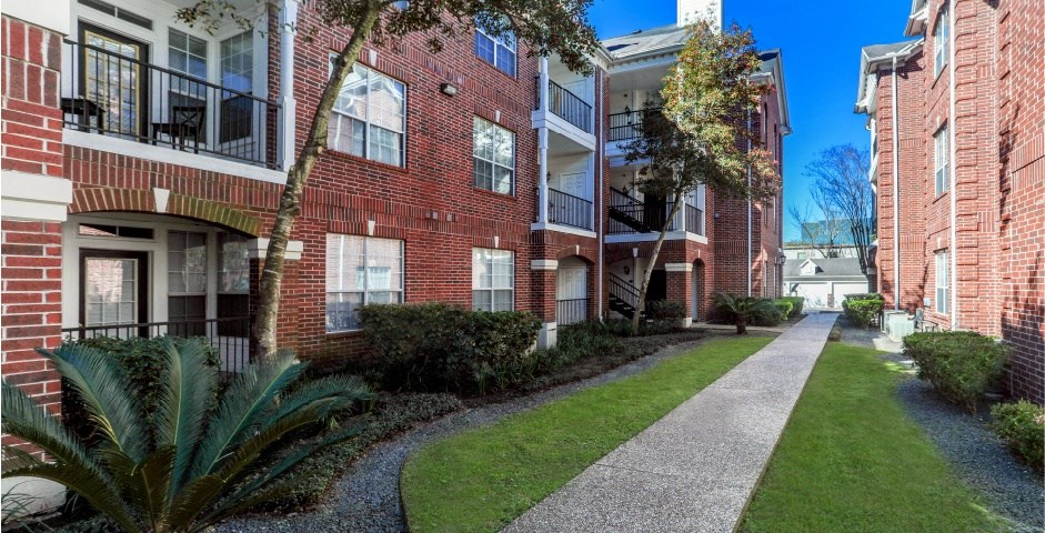 Luxury apartments with brick exteriors, beautiful landscaping, and patios with extra storage and French doors at Tuscany Apartments in Houston.