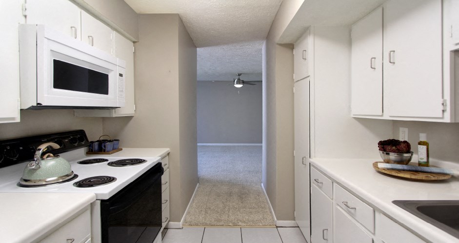 Bright white kitchen with gray wall color, white kitchen cabinets, lots of cabinet space, lots of counter space, spacious dining room and porcelain tile floors at The Inverness Apartments in La Vista, Nebraska