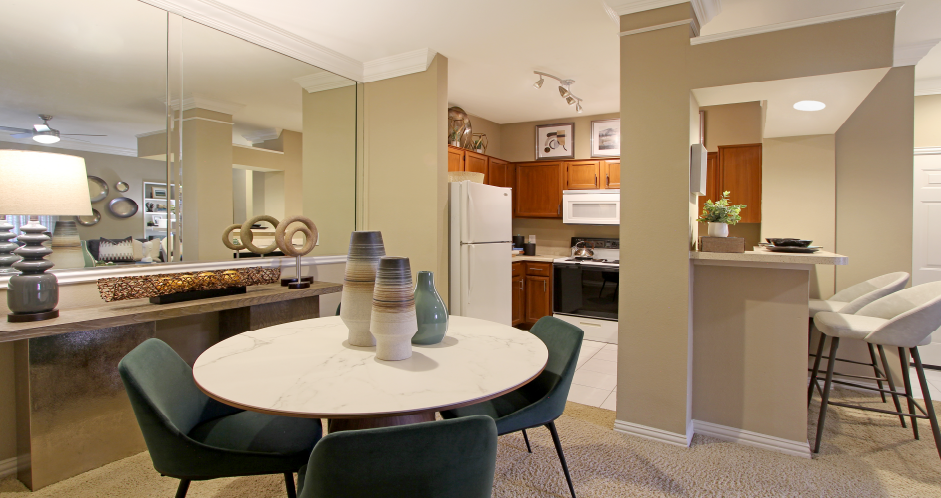 Dining room with mirror accent wall and U-shaped kitchen with breakfast bar at The Dorchester Apartments in north Dallas.
