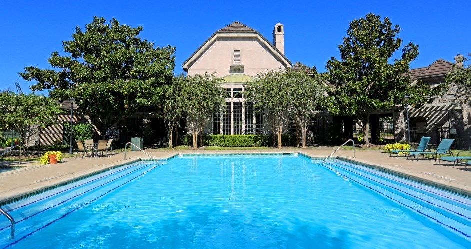 Luxury resort-style swimming pool with poolside lounges chairs, beautiful landscaping, lush landscaping and scenic views at Village on the Parkway Apartments.