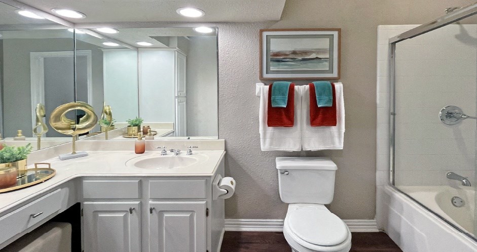 Luxury apartments with wood grain plank floors, extra cabinet space, white cabinets, built-in vanity, oval soaking tub, and glass shower at Lenox Village Apartments in Lincoln, NE