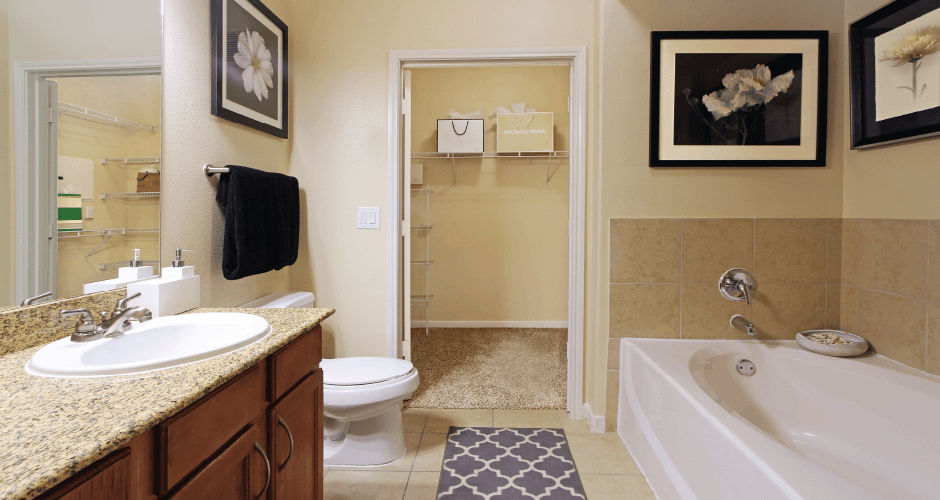 Spacious master bathroom with oval soaking tub, separate glass shower, and attached large walk-in closet at The Voss Apartments in Houston.